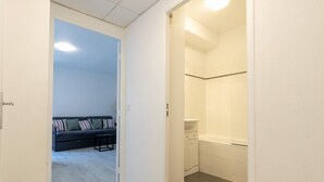 A hallway leading to a bathroom with a bathtub and a seating area with a sofa and pillows. - Scenic Riviera Home Near sea (Grasse)