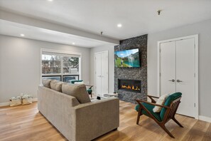Ein modernes Wohnzimmer mit einer Couch, einem an einer Steinwand montierten Fernseher, einem Kamin und einer Tür.