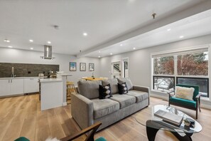 Eine moderne Küche mit weißen Schränken, einem grauen Sofa und einem Essbereich mit Holztisch.
