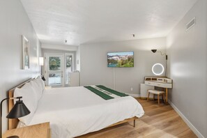 Ein Schlafzimmer mit Bett, Schreibtisch, Stuhl, Fernseher und Fenster.