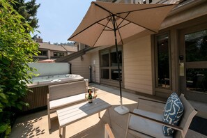 Un patio con un jacuzzi, mobiliario exterior y una sombrilla grande.