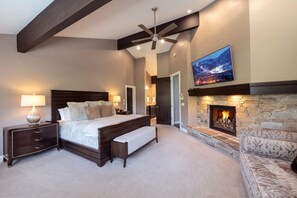 A bedroom with a large bed, a nightstand, a bench, a fireplace, a ceiling fan, and a TV mounted on the wall. - Spacious 5BR, 5BA Deer Valley Nordic Village Haus—ideal mountain retreat for 12. (Park City)