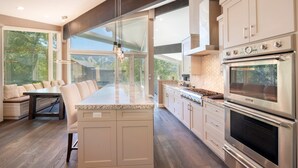 Een moderne keuken met een groot eiland, roestvrijstalen apparatuur en uitzicht op de omgeving.