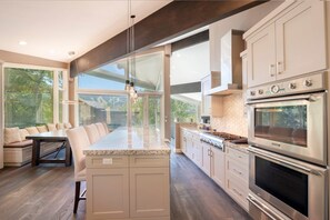 A modern kitchen with a large island, built-in oven, and a dining area with a bench. - Spacious 5BR, 5BA Deer Valley Nordic Village Haus—ideal mountain retreat for 12. (Park City)