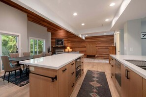 A modern kitchen with wooden cabinetry, a central island, and a dining area with chairs. - Spacious 4BR retreat in Deer Valley with stunning mountain views. (Park City)