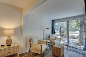 Ein Zimmer mit Glastür, die zu einem Außenbereich führt, einer Lampe, zwei Korbstühlen, einem kleinen Tisch und einem Holzboden.