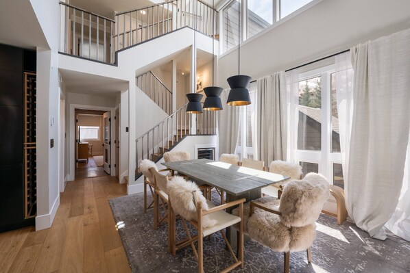 A spacious dining area with a high ceiling, a staircase, and large windows. - Modern Park City Retreat | Private Hot Tub Near Slopes (Park City)