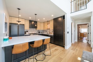 A modern kitchen with a large island, bar stools, and a view to the upper level. - Modern Park City Retreat | Private Hot Tub Near Slopes (Park City)