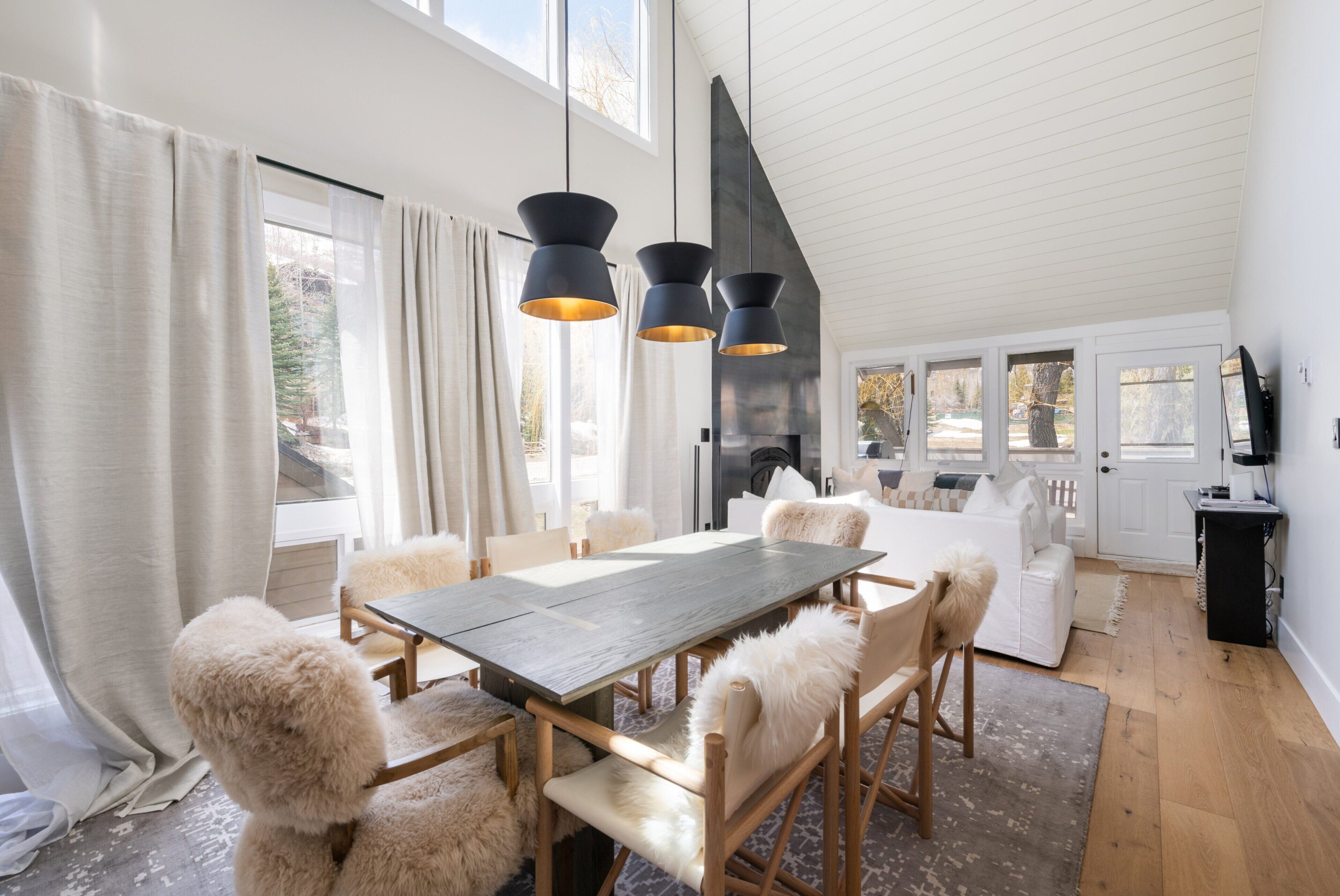 A modern dining area with a wooden table and chairs, a fireplace, and a large window with curtains.