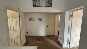 Un corridoio con porte bianche, tappeto color beige e un quadro appeso al muro.