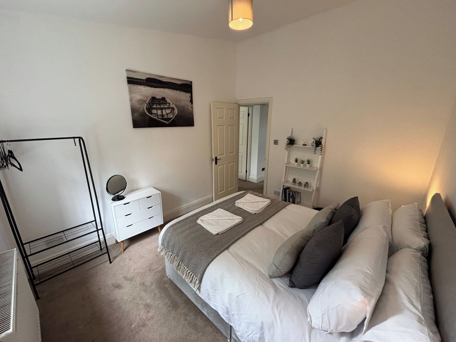 Une chambre à coucher comprenant un lit, une commode, un miroir, une armoire, une porte et une étagère avec des plantes.