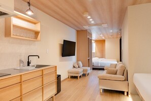 Een moderne hotelkamer met een houten vloer, een kitchenette met een spoelbak en kastjes, een flatscreen televisie, een bank en een bed.