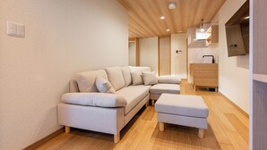 A modern living room with a sofa, ottoman, wooden flooring, recessed ceiling lights, and a built-in TV. - 【新築OPEN】浅草寺徒歩1分! 雷門20秒/檜風呂・Simmons/最大収容人数8名/渋谷新宿浅草 (Tokyo)