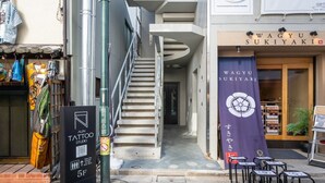 A narrow alleyway with a staircase leading to a building. A tattoo studio sign is visible on the left, and a banner for WAGYU SUKIYAKI is on the right. - 【新築OPEN】浅草寺徒歩1分! 雷門20秒/檜風呂・Simmons/最大収容人数8名/渋谷新宿浅草 (Tokyo)