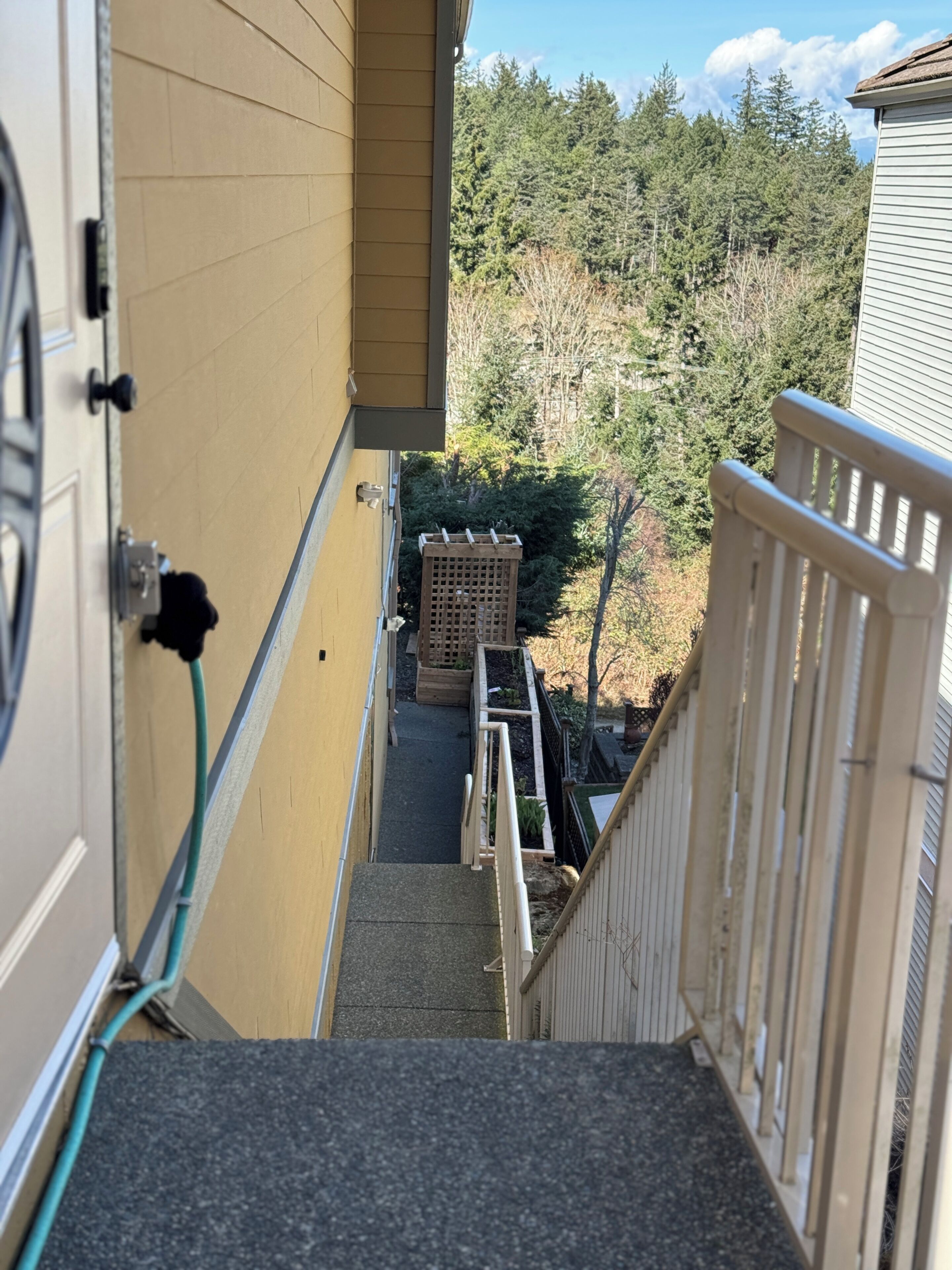 A narrow outdoor stairway leading to a wooden deck, surrounded by a fence and a wooden planter.. Enjoy a bright and comfortable 2‑bedroom suite with a private entrance, full kitchen, and one bathroom. The space accommodates up to six guests and includes a cozy living area, smart TV, Wi‑Fi