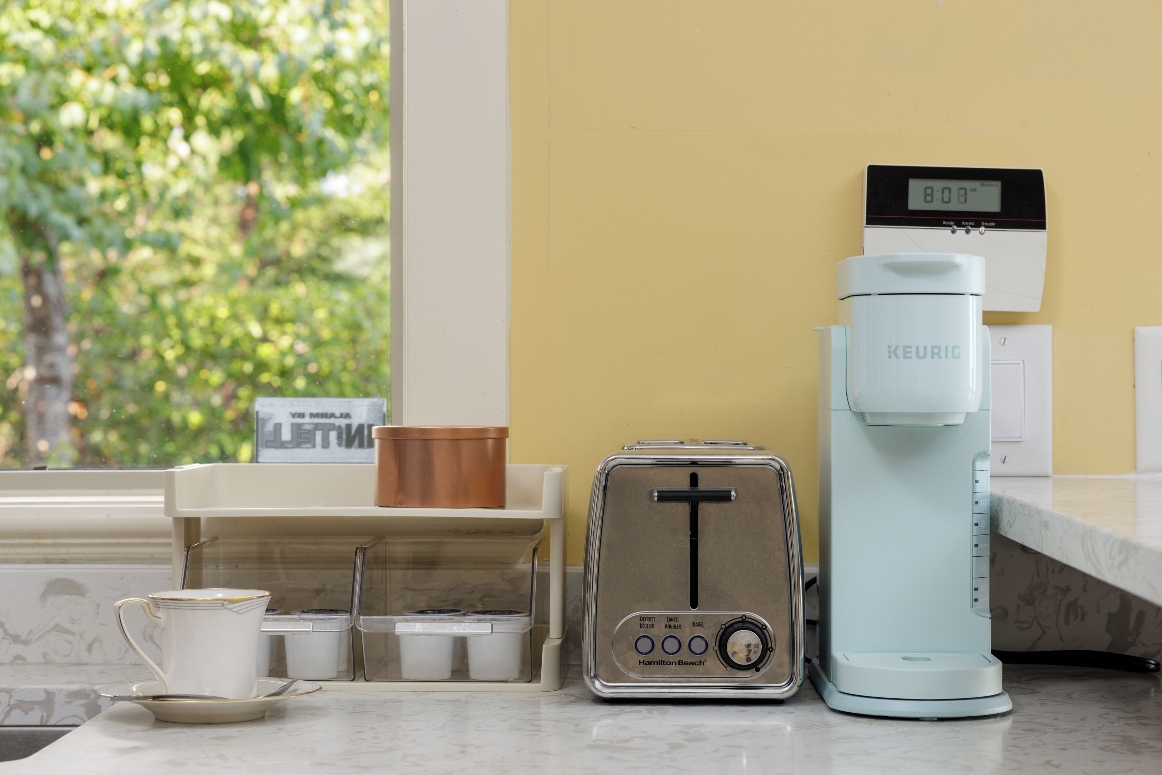 Een keukenblad met een Keurig koffiezetapparaat, een broodrooster en een koffiekop.