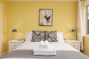 Una habitación de hotel con cama, dos mesitas de noche, un cuadro y una ventana con cortinas.