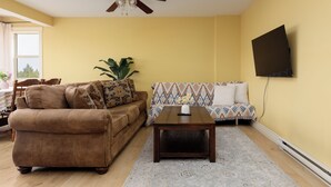 A living room with a brown sofa, a patterned couch, a wooden coffee table, and a ceiling fan.
