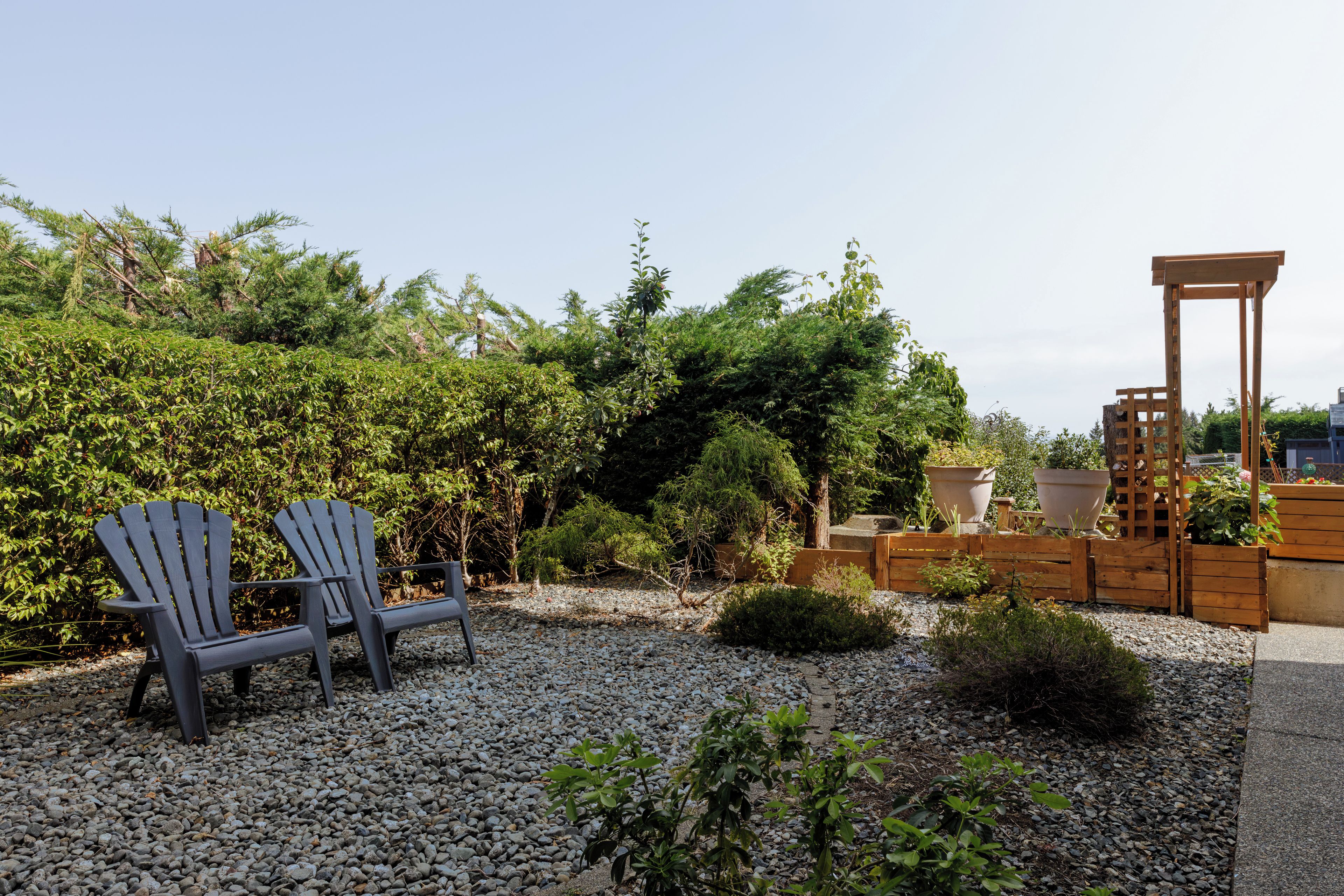 Un jardín con dos sillas Adirondack, una pérgola de madera y diversas plantas.