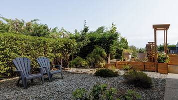 Un jardín con dos sillas Adirondack, una pérgola de madera y diversas plantas.