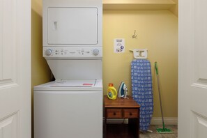 A laundry area with a washing machine, a dryer, a table with cleaning supplies, and a ironing board. - Enjoy a bright and comfortable 2‑bedroom suite with a private entrance, full kitchen, and one bathroom. The space accommodates up to six guests and includes a cozy living area, smart TV, Wi‑Fi (Nanaimo)