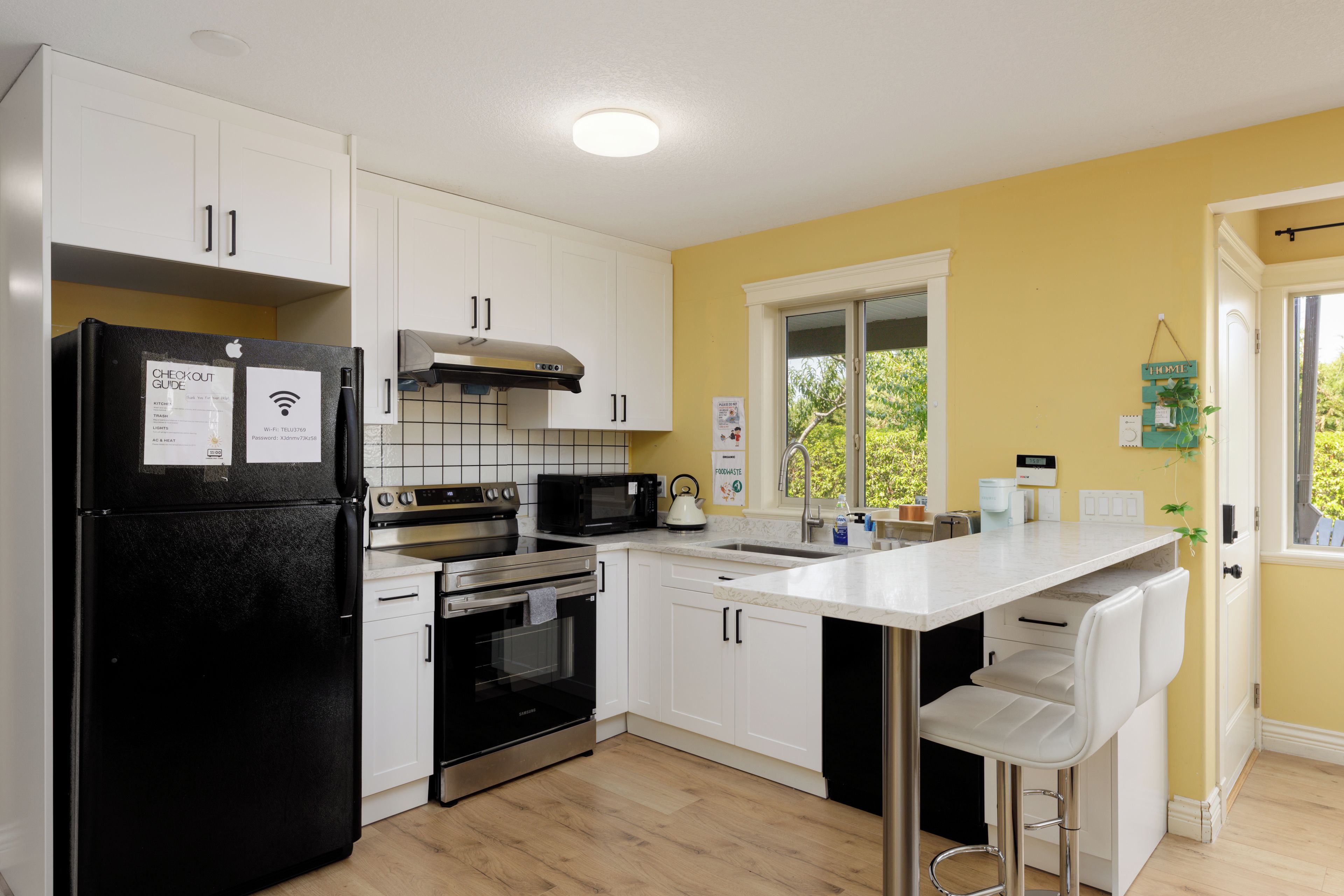 A modern kitchen with white cabinetry, a black refrigerator, stainless steel appliances, and a yellow accent wall.