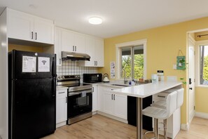 A modern kitchen with white cabinetry, a black refrigerator, stainless steel appliances, and a yellow accent wall. - Enjoy a bright and comfortable 2‑bedroom suite with a private entrance, full kitchen, and one bathroom. The space accommodates up to six guests and includes a cozy living area, smart TV, Wi‑Fi (Nanaimo)