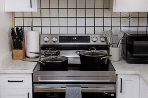 Una cocina con estufa de acero inoxidable, dos ollas, un tostador y un juego de cuchillos.