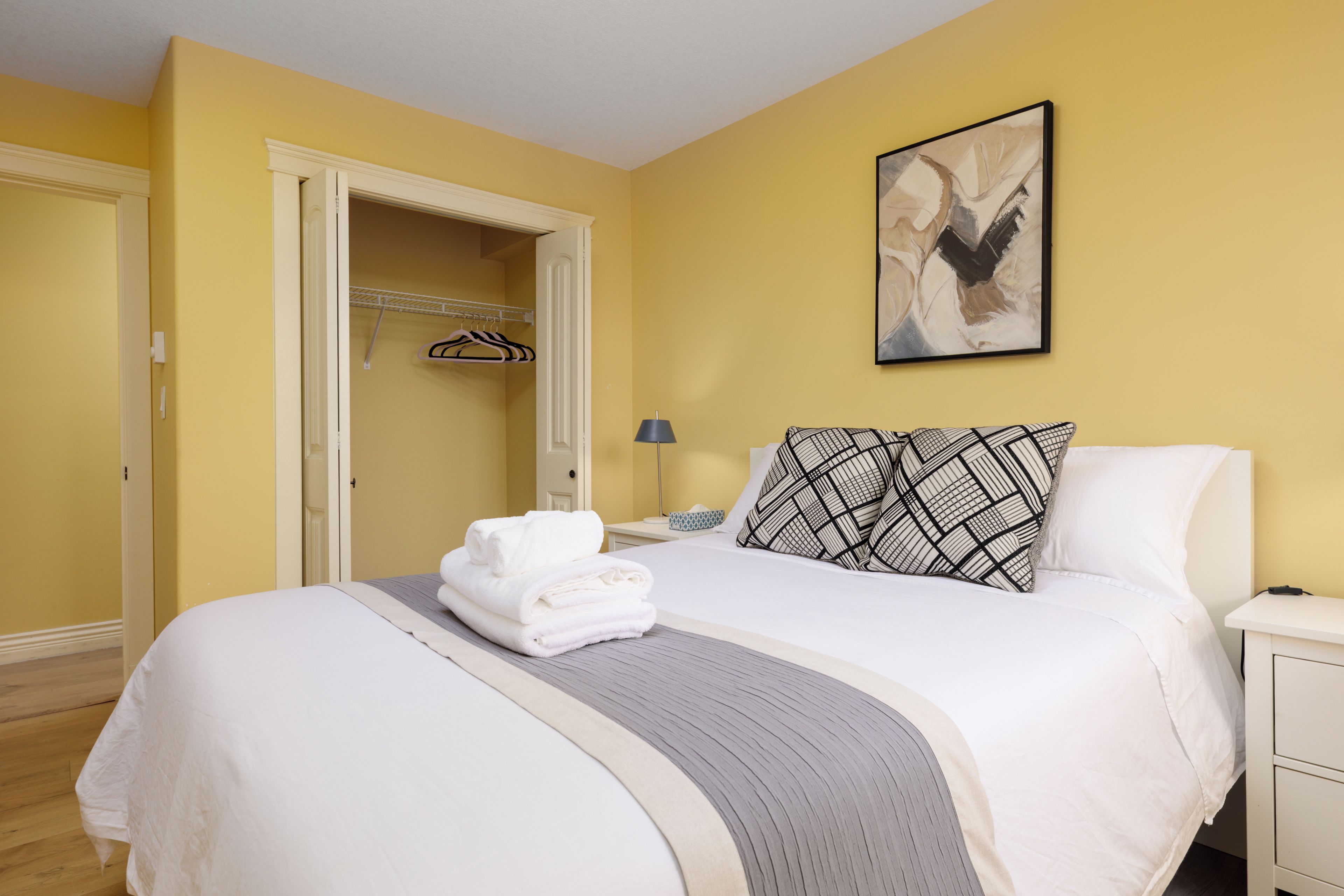 Habitación de hotel con una cama, una mesita de noche, una lámpara, una obra de arte enmarcada y un armario.