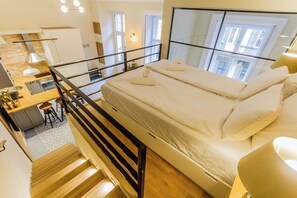 A modern bedroom with a bed, a staircase, a kitchen area, and a view of the city. - The Muzeum Living ~ Boutique City Stay Spacious 2BR in Downtown (Budapest)
