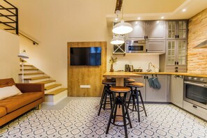 A modern kitchen with a wooden countertop, bar stools, a TV, and a stone wall. - The Muzeum Living ~ Boutique City Stay Spacious 2BR in Downtown (Budapest)