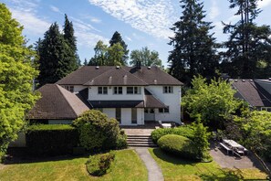 A two-story house with a front porch, a covered patio, and a well-maintained lawn. - Cozy Vintage 7BR Home with Sunny Backyard (Vancouver)
