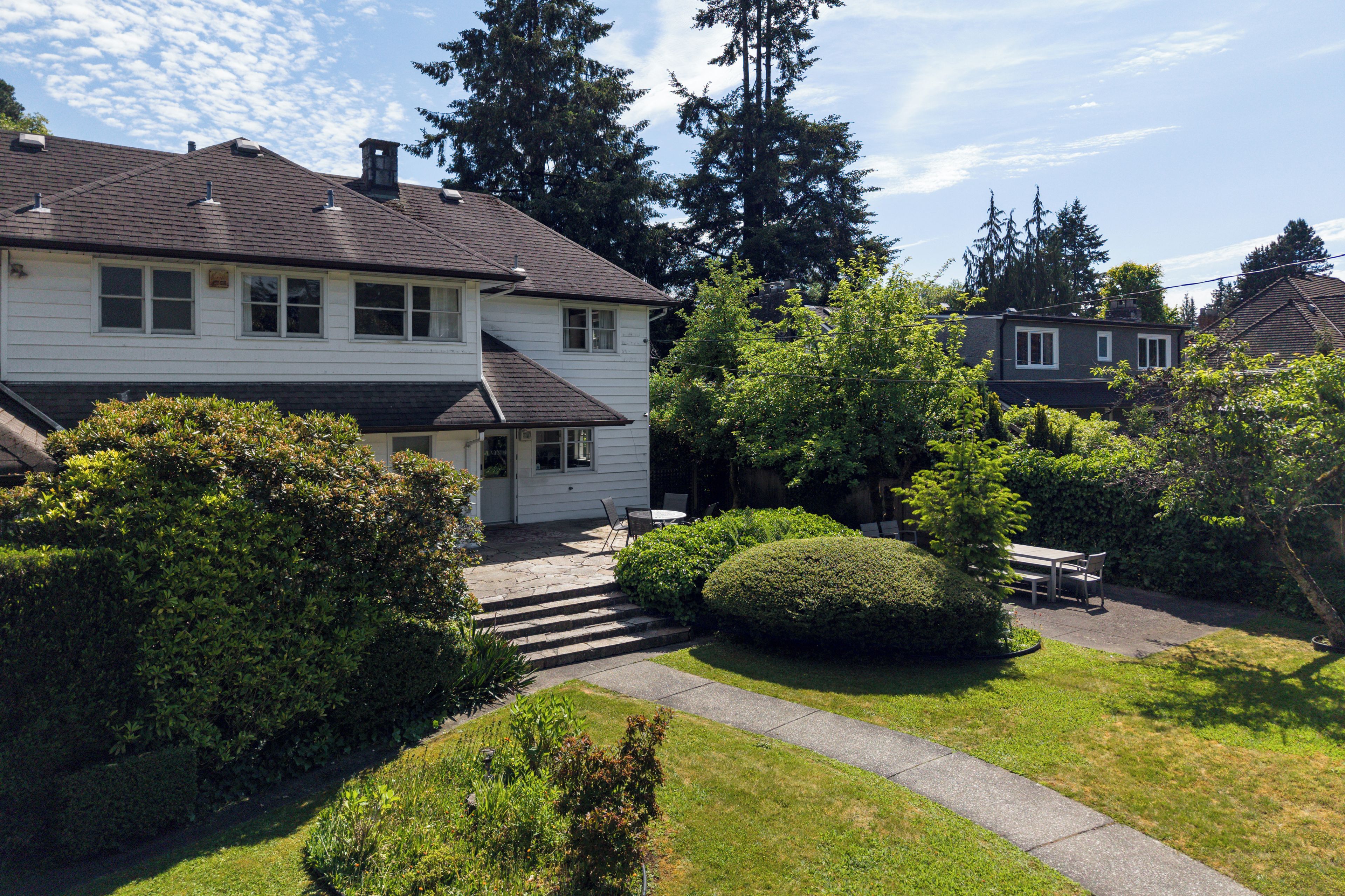 A two-story residential house with a front porch, a stone pathway leading to the entrance, and a well-maintained garden with various shrubs and a small tree.