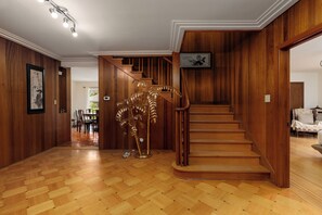 A wooden interior with a staircase, a dining area, and a decorative golden plant. - Cozy Vintage 7BR Home with Sunny Backyard (Vancouver)