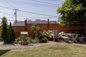 Ein Garten mit Holzzaun, Grill, Picknicktischen und verschiedenen Pflanzen und Blumen.