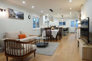 Een moderne woonkamer met een bank, stoelen, een eettafel en een keuken met kastjes en een televisie.
