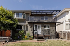 A two-story residential building with a covered patio, a wooden fence, and a picnic table. - Spacious 6BR Home Near DT and 15 mins to YVR (Vancouver)
