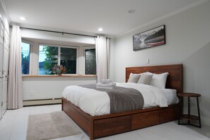 Een slaapkamer met een groot bed, een raam met gordijnen, een klein tafeltje en een schilderij aan de muur.
