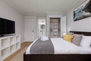 A bedroom with a bed, a TV, a walk-in closet, and a bathroom. - Spacious 6BR Home Near DT and 15 mins to YVR (Vancouver)