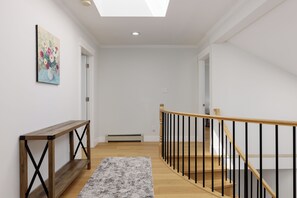 Ein Flur mit einer hölzernen Bank, einem Teppich und einer Treppe mit schwarzen Geländern.