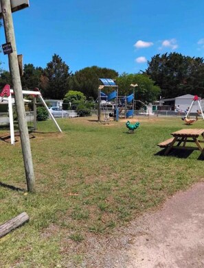 A playground with a slide, swings, and a green dinosaur toy. - Mobile home rental between la Palmyre and les mathes (Les Mathes)