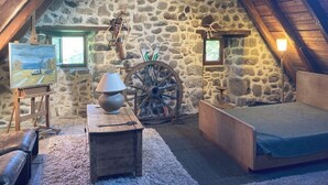 Ein rustikaler Dachbodenraum mit Steinwand, einem hölzernen Bett, einem Gemälde an der Wand und einem Holztisch mit Lampe.