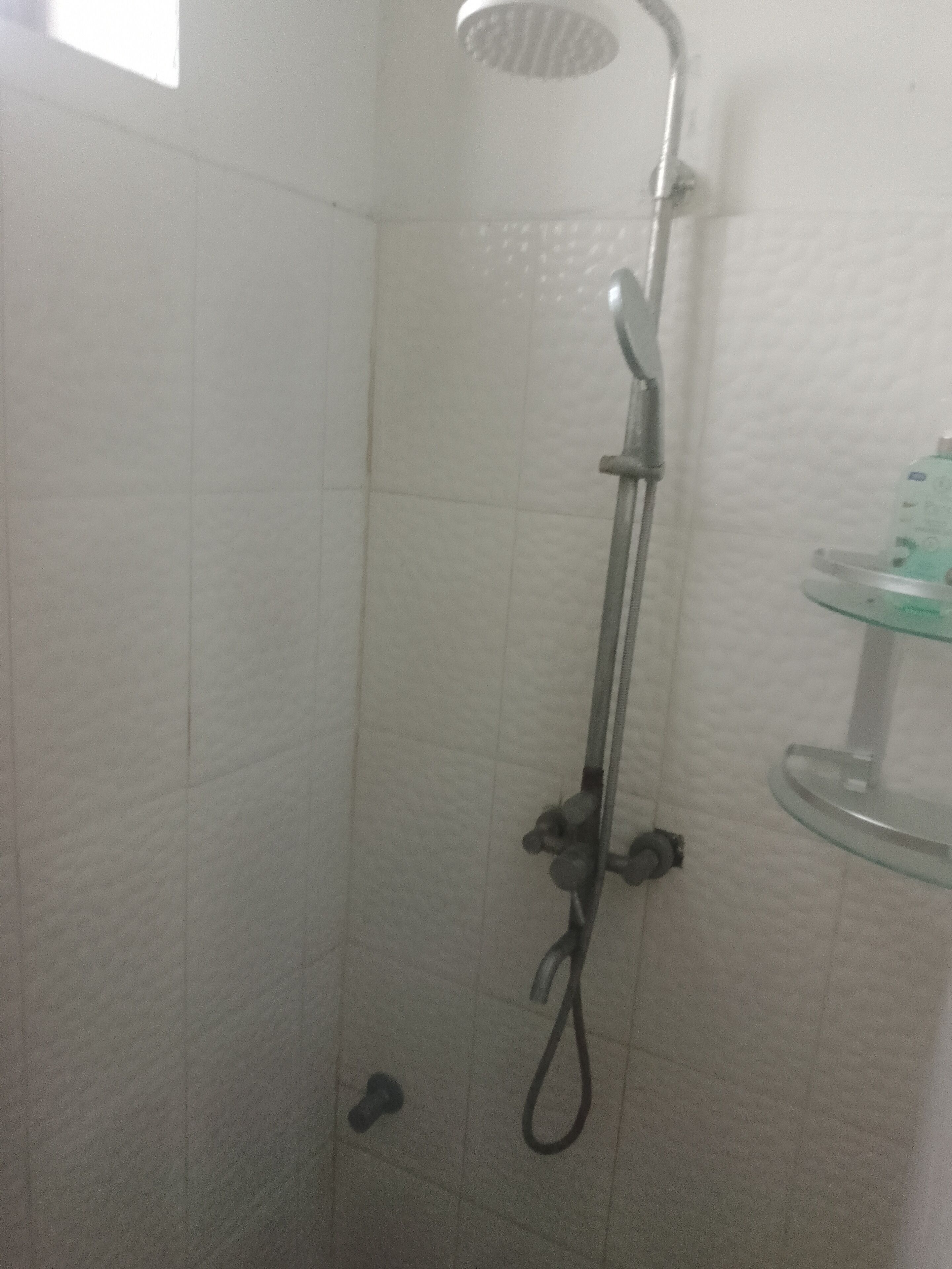 A shower with a handheld showerhead, a wall-mounted faucet, and a glass shelf with toiletries.