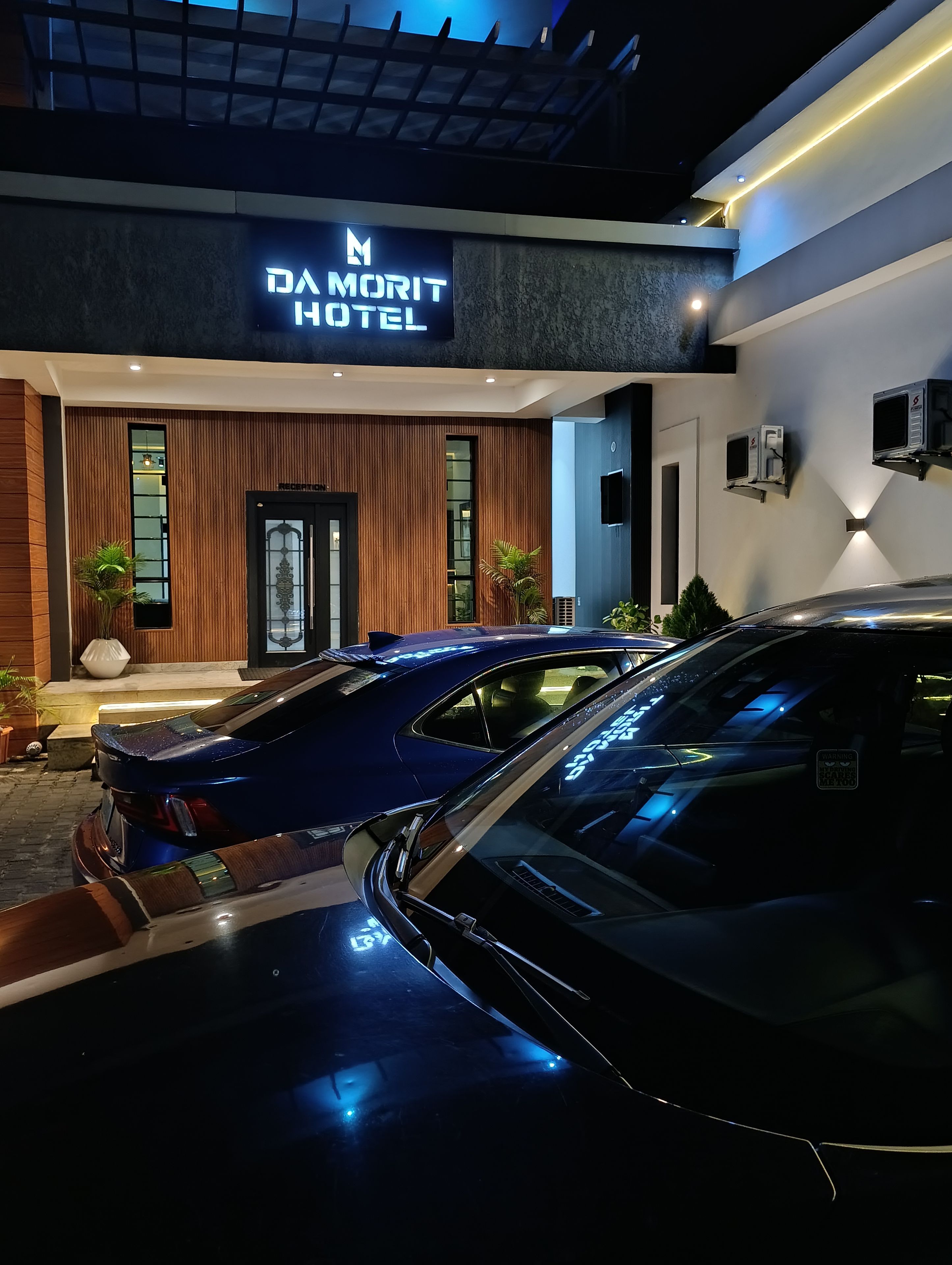 Ein moderner Hotelzugang mit einem Schild, zwei Autos vor der Einfahrt und einem verschlossenen Zugang.
