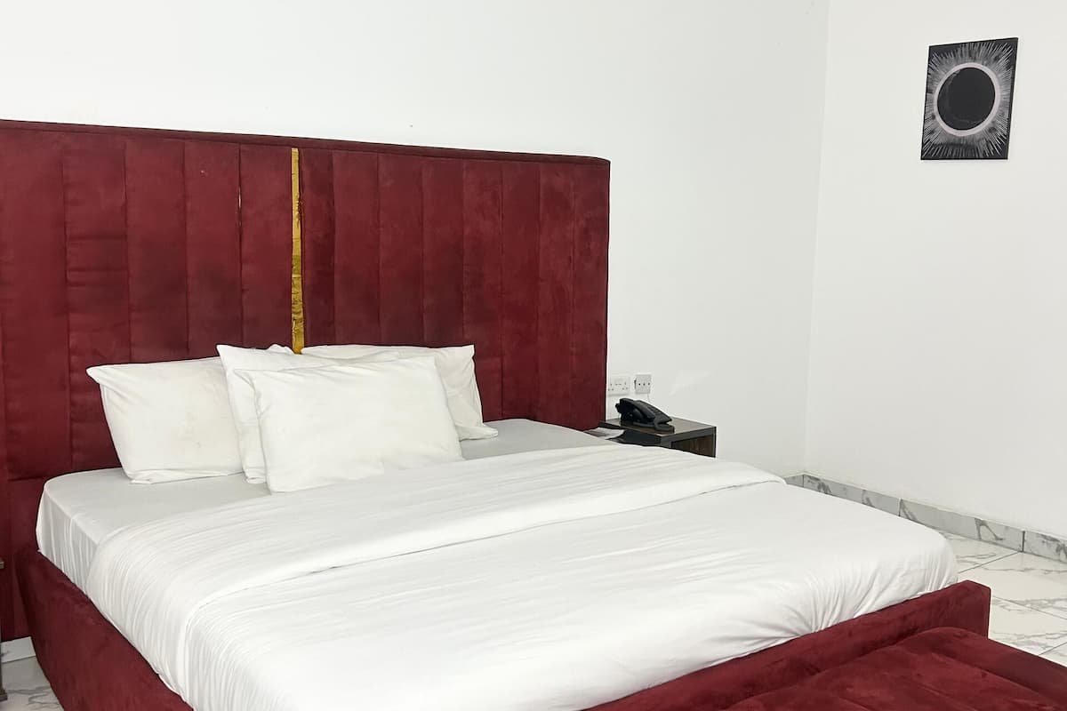 A bedroom with a large bed, a red headboard, white bedding, a bedside table with a phone, and a wall-mounted light fixture.