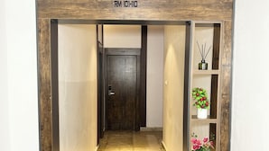 A hallway with a wooden door labeled 'RM 101-110,' a marble floor, and a shelf with potted plants.