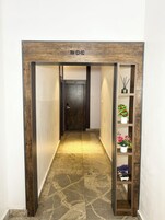Um corredor com porta de madeira identificada como 'RM 101-110', piso de mármore e uma prateleira com plantas em vasos.