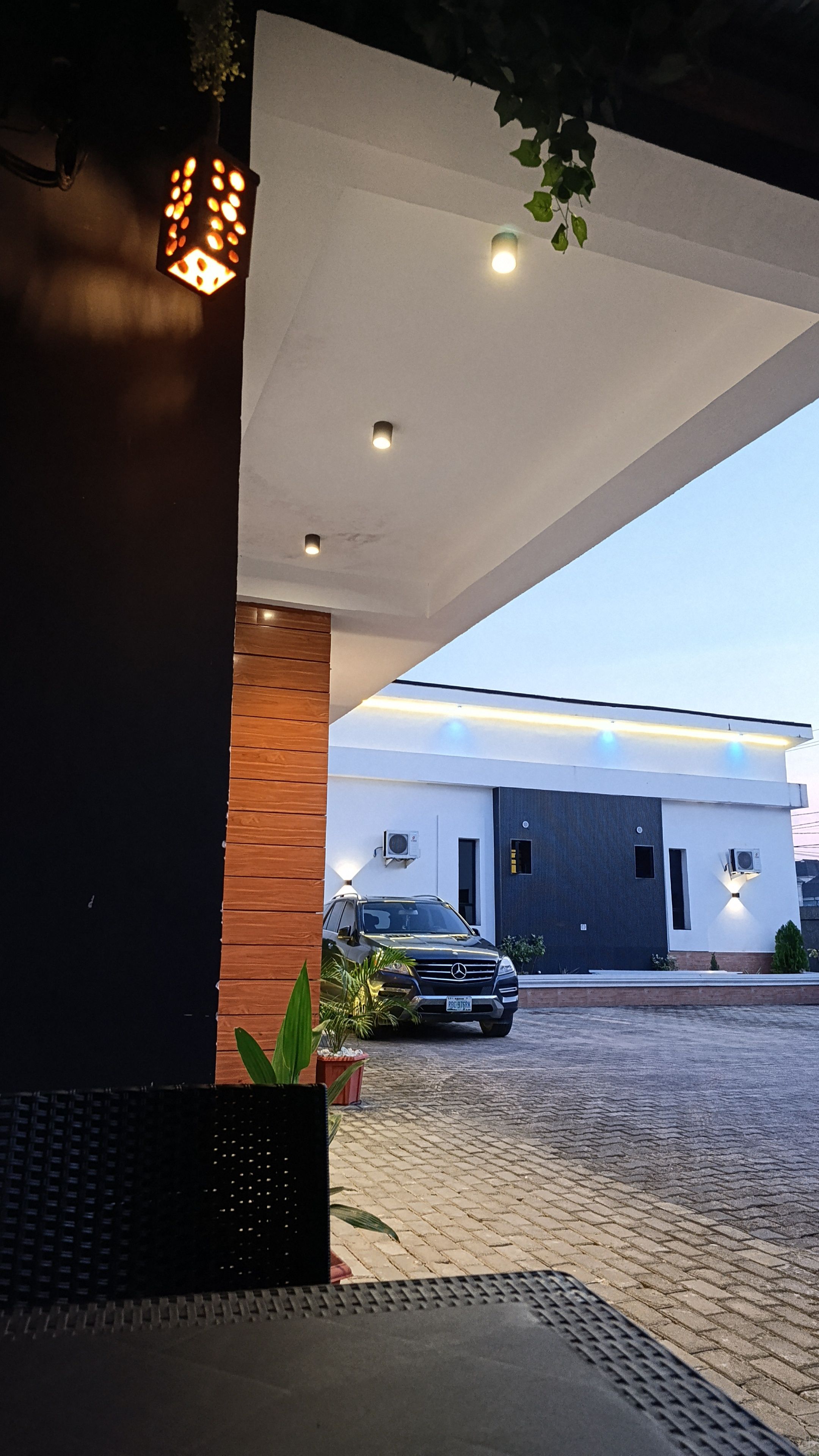 A modern building with a paved driveway, a parked car, and a hanging light fixture.