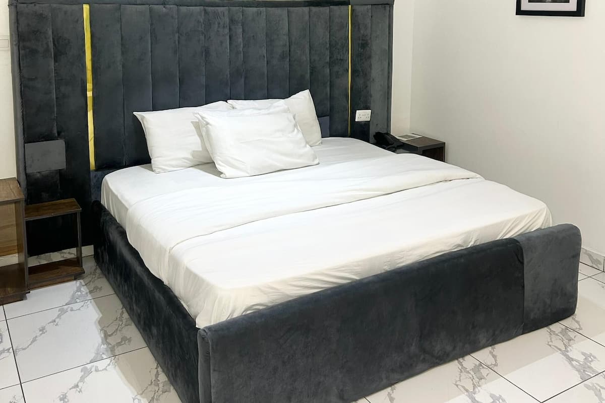 A bedroom with a large bed, a headboard, a bedside table, a nightstand, and a framed picture on the wall.