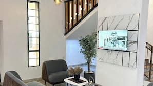 A modern living room with a sofa set, a coffee table, a potted plant, and a television mounted on the wall.
